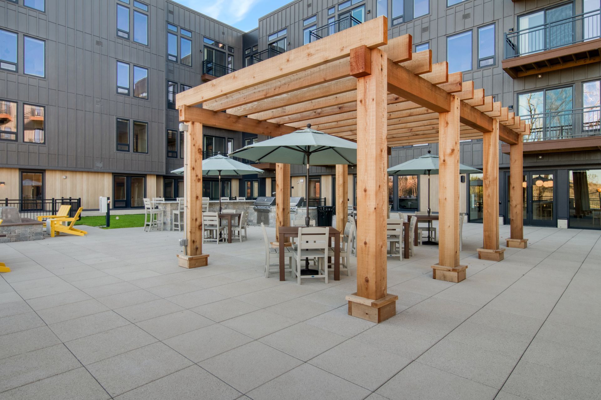 A wooden pergola with tables and umbrellas in front of a building.