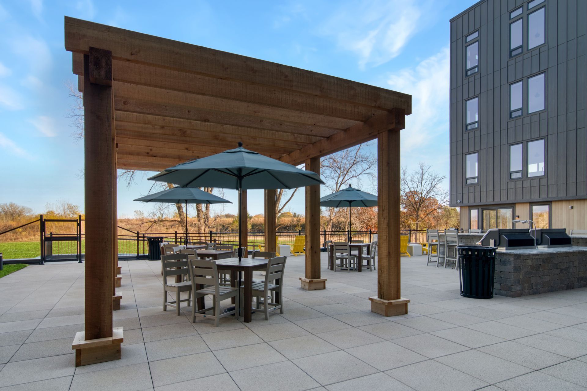 A patio with tables and umbrellas under a wooden pergola.