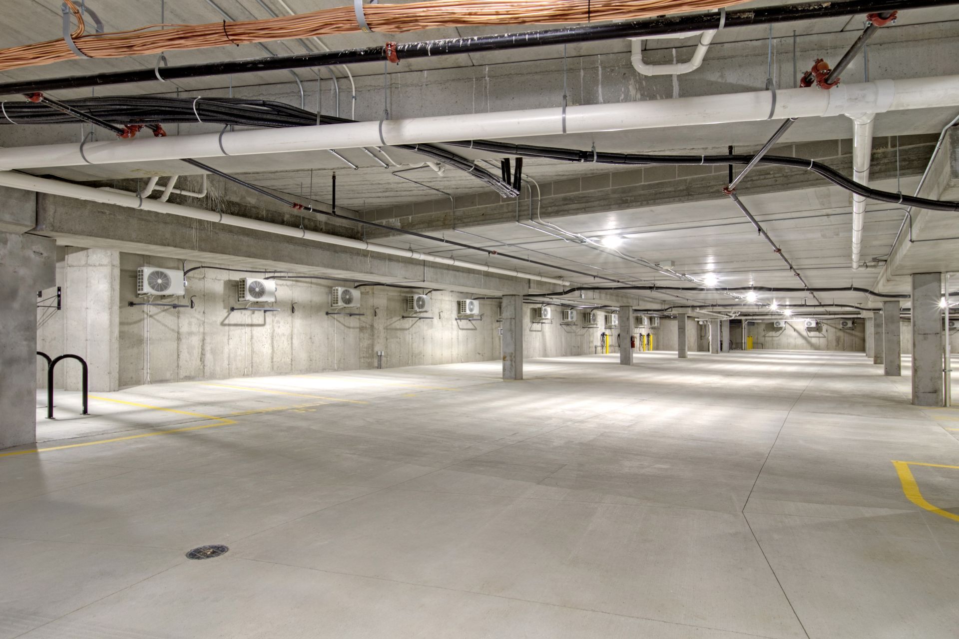 An empty parking garage with a lot of pipes hanging from the ceiling.
