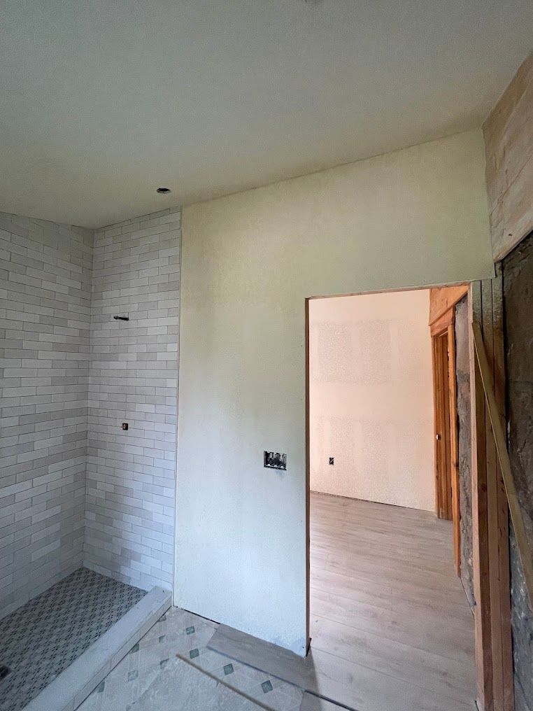 A bathroom under construction with a walk in shower and a door leading to another room.