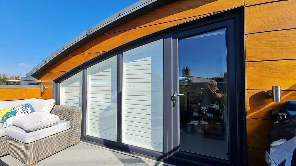 Sliding glass doors on a deck, wooden siding, gray trim, and outdoor seating.