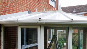 White conservatory roof with ornate details and clear panels, attached to a brick building.