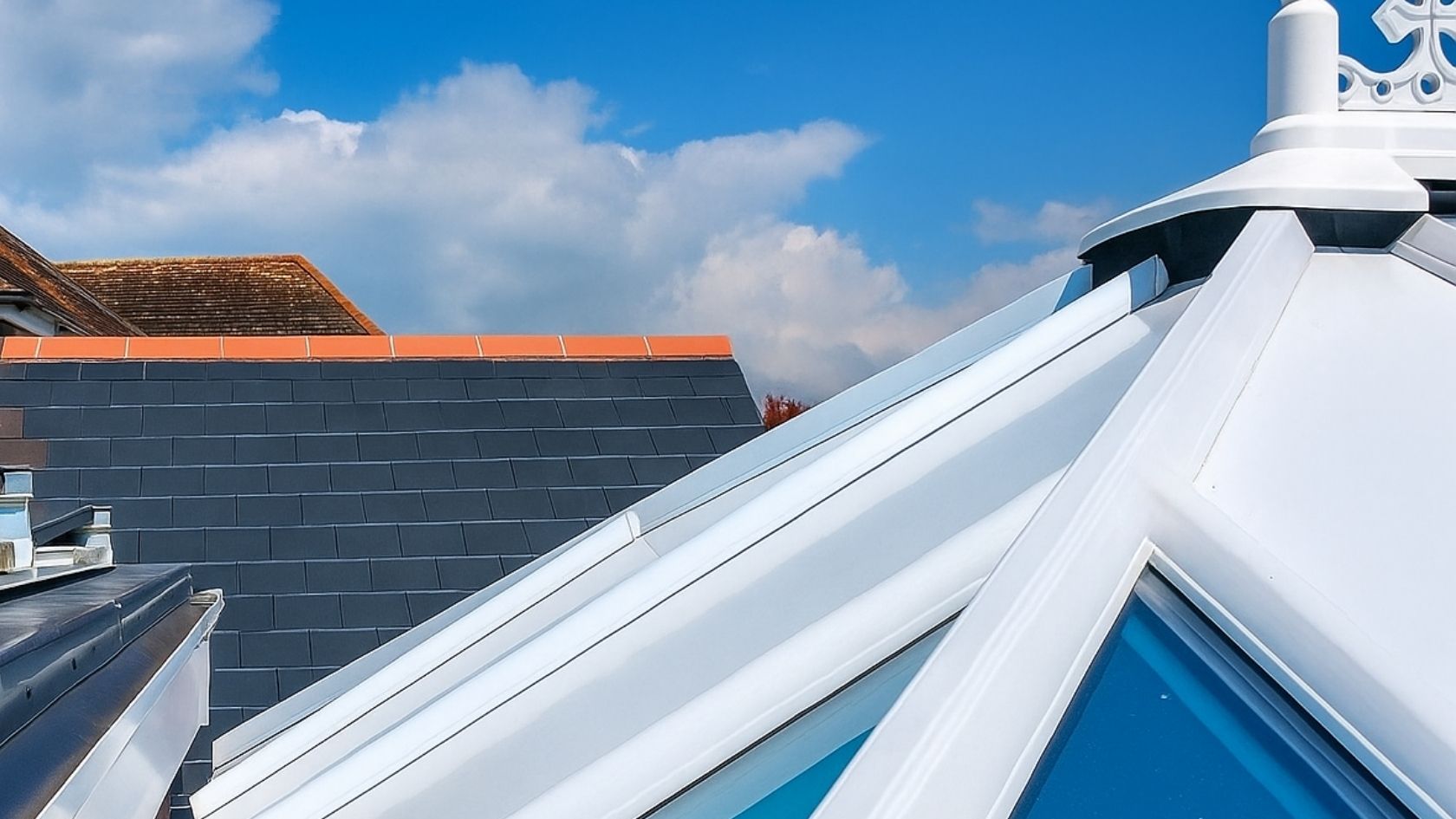 Close-up of a white, geometric skylight, next to blue sky and a dark gray tiled roof.