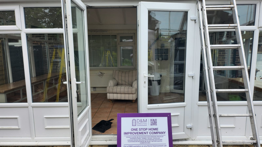 White-framed sunroom with open doors. Ladder propped up, chair inside. Sign on the ground.