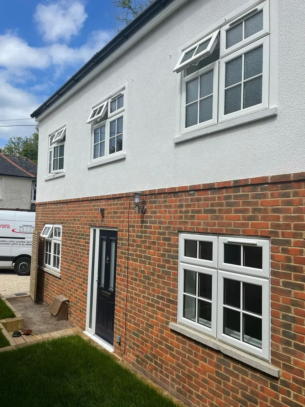 Two-story building with white stucco upper level and brick lower level; white-framed windows; dark door.