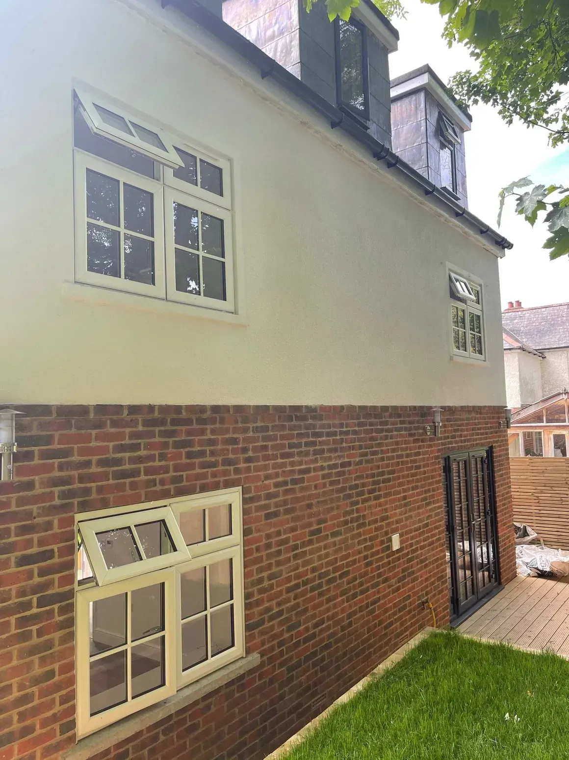 Two-story building with brick base and white stucco upper walls, white windows. Green grass in foreground.