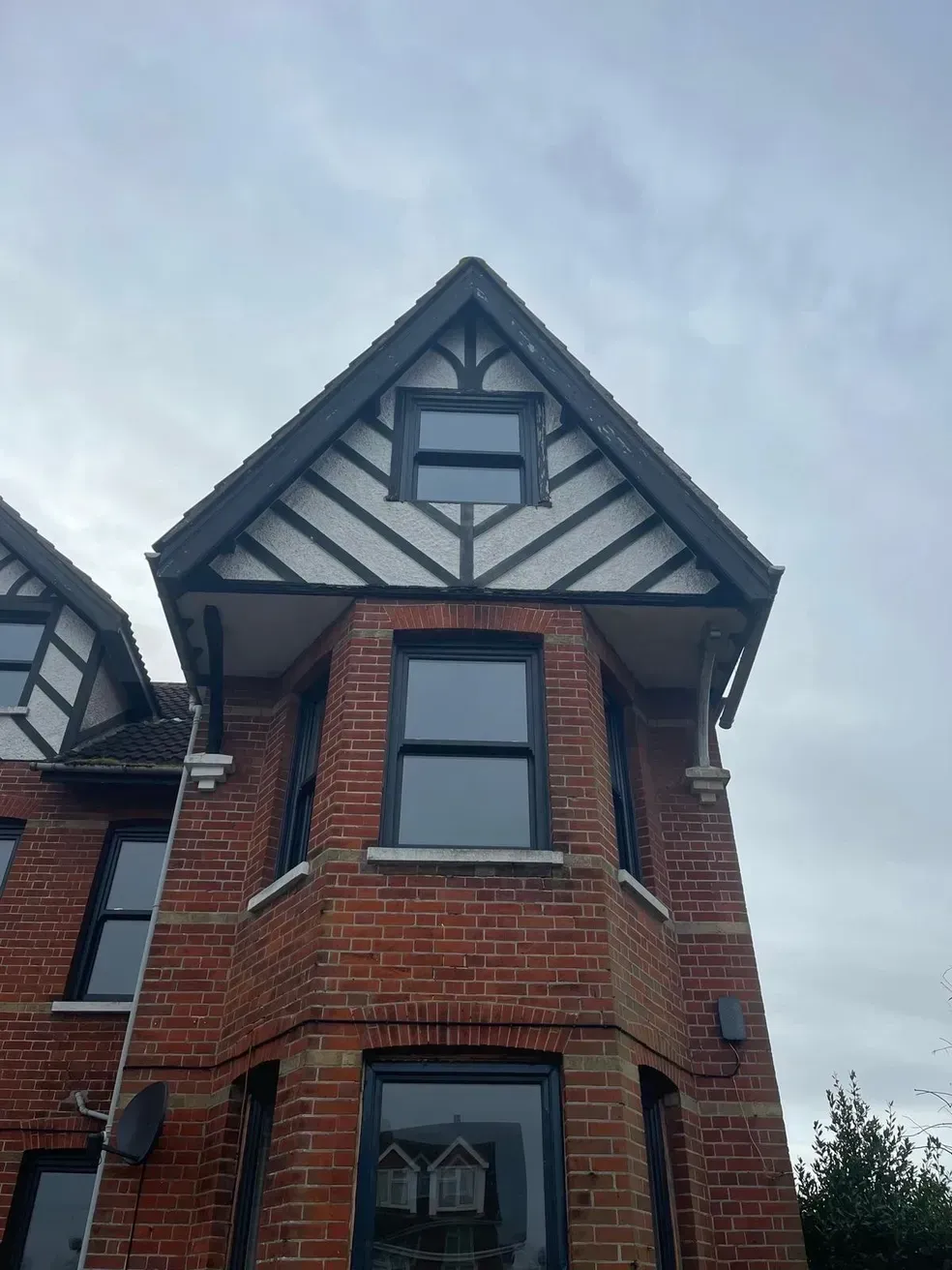 Red brick house with black-framed windows and a triangular roof with white and black accents under a cloudy sky.