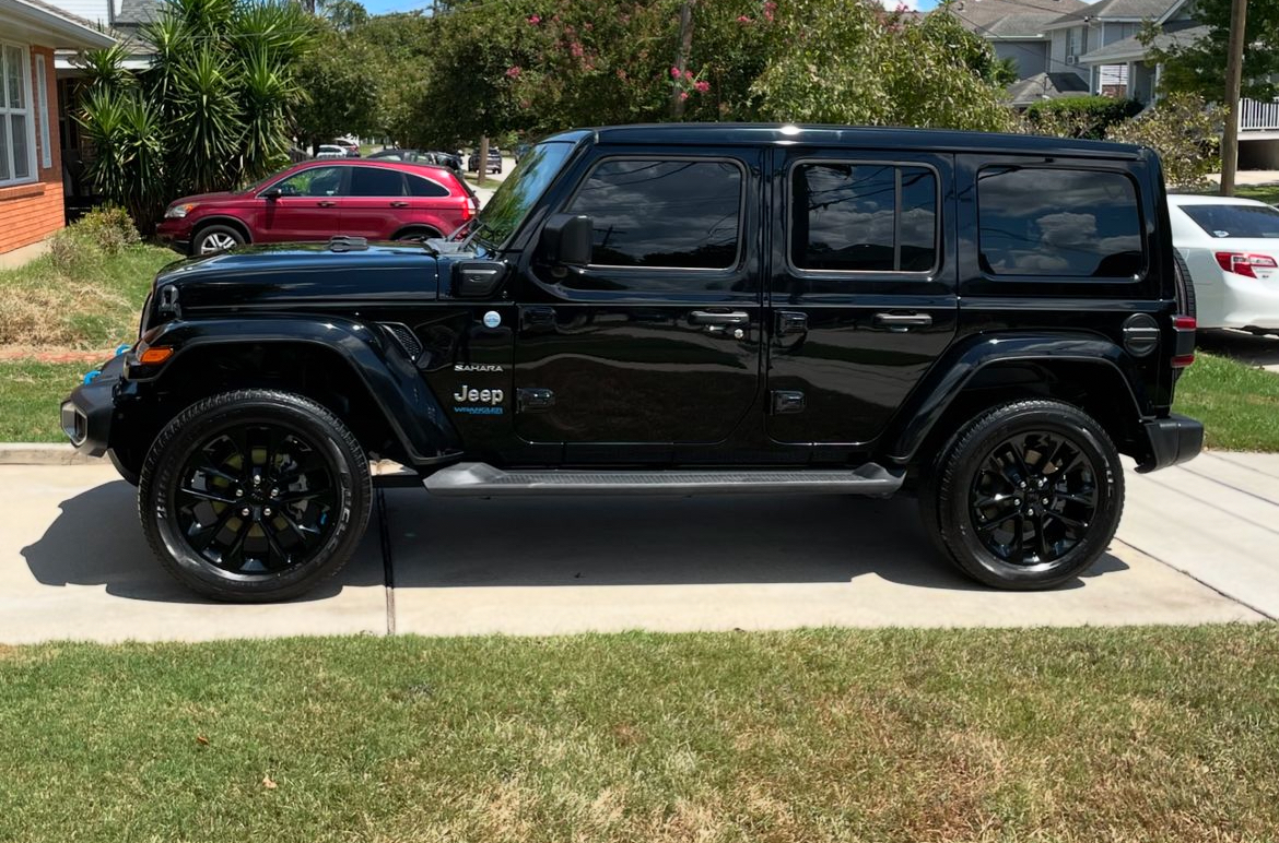 A black jeep wrangler is parked on the side of the road in front of a house.
