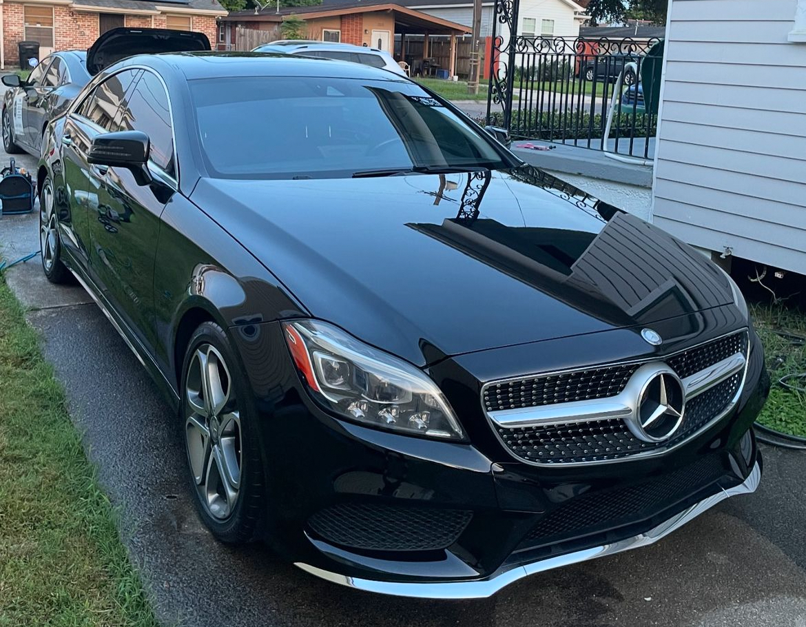 A black mercedes benz is parked in a driveway next to a house.