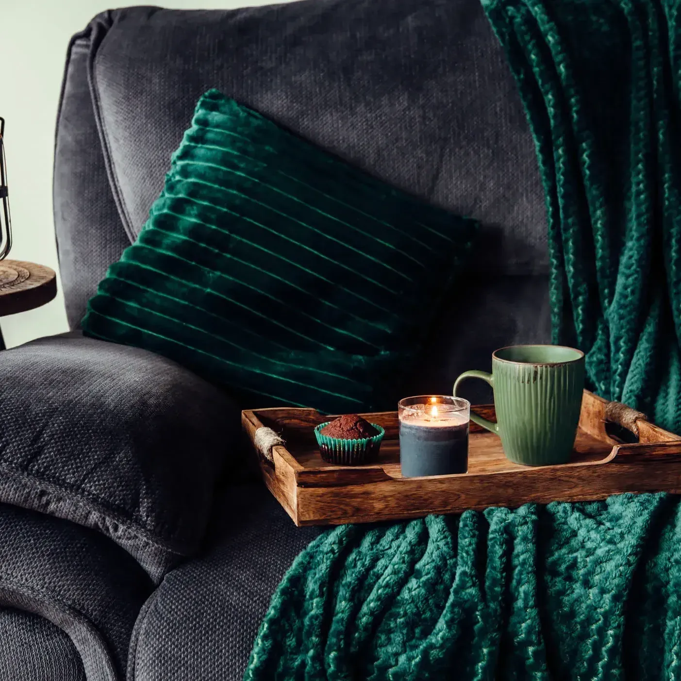 A chair with a green blanket and a tray with a candle and cupcakes on it.