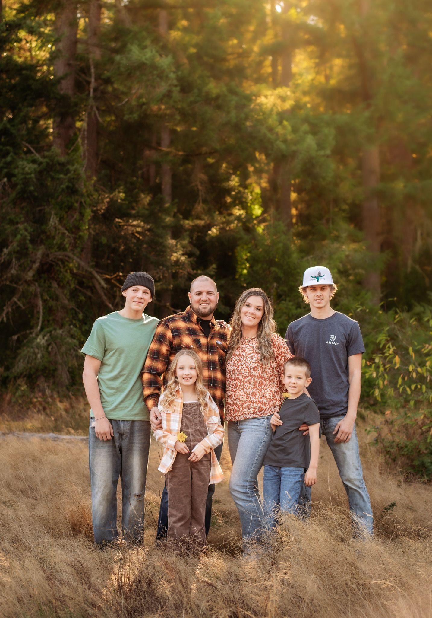 Five people standing in tall grass in a sunlit forest clearing, posing together.