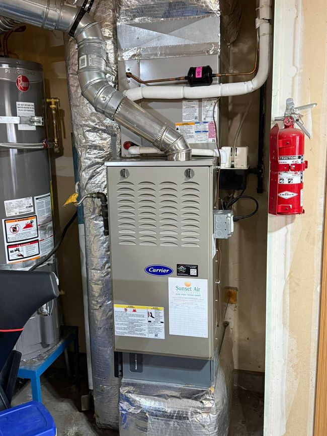 Gas furnace and ductwork in a utility closet, with a red fire extinguisher on the wall.