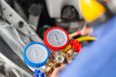 Mechanic adjusting red and blue car AC manifold gauges under the hood