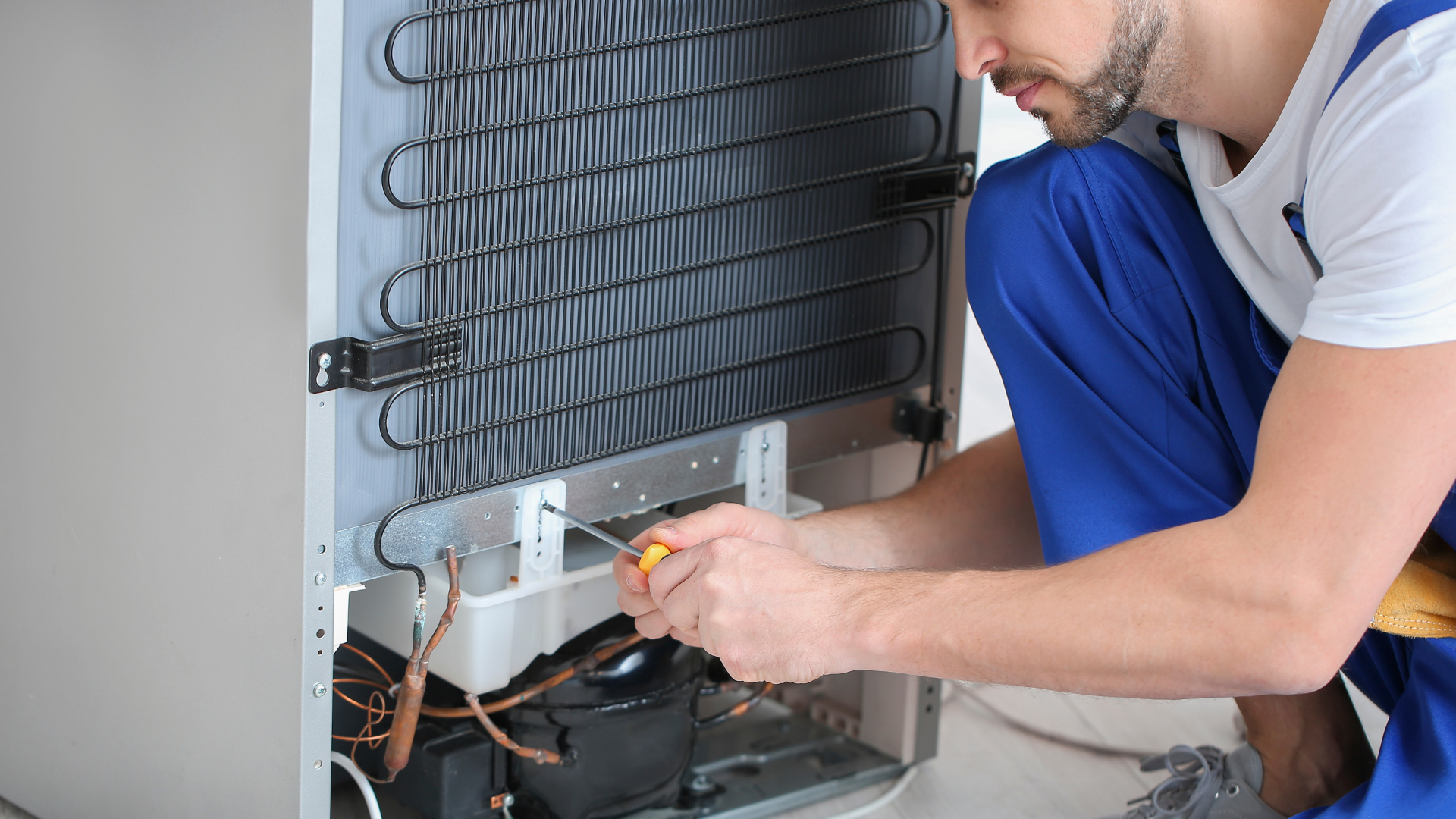 A man is fixing a refrigerator with a screwdriver.
