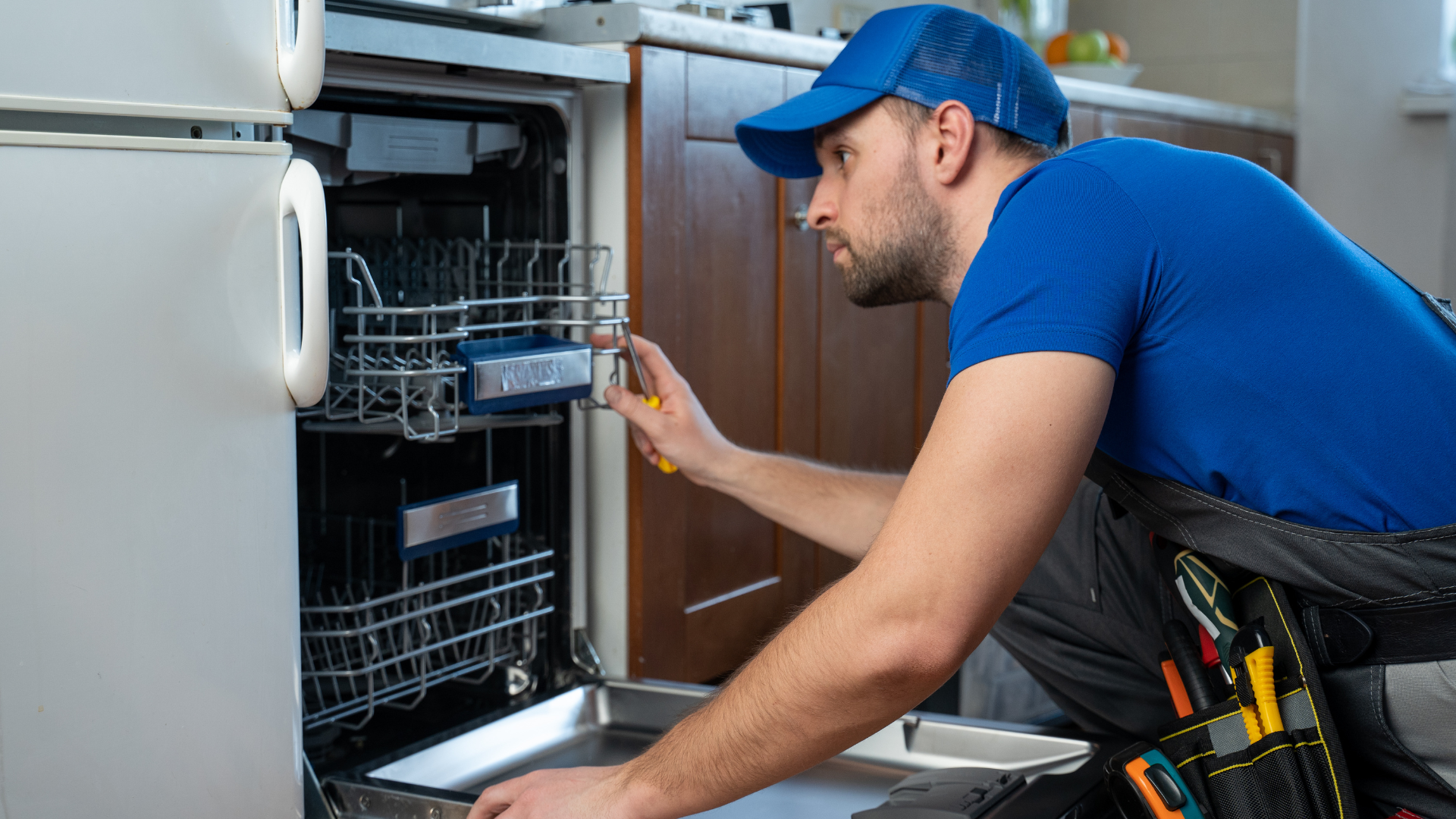 A man is fixing a dishwasher in a kitchen.