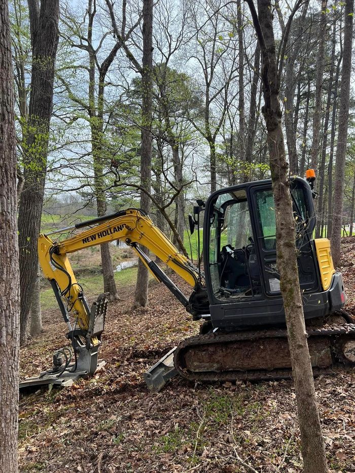 a yellow excavator is sitting in the middle of a forest .