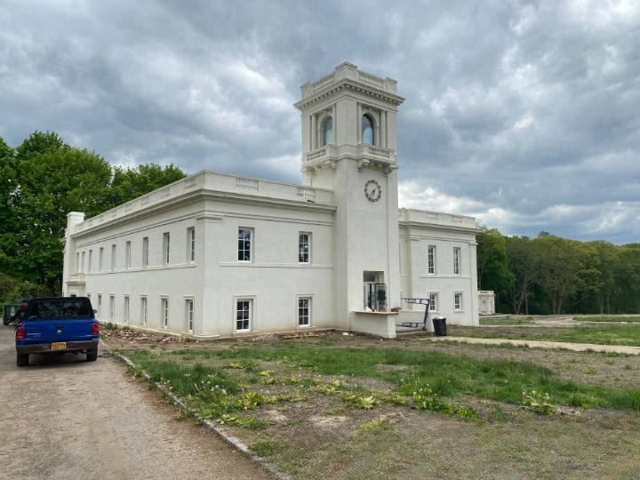 A blue truck is parked in front of a large white building with a clock tower.