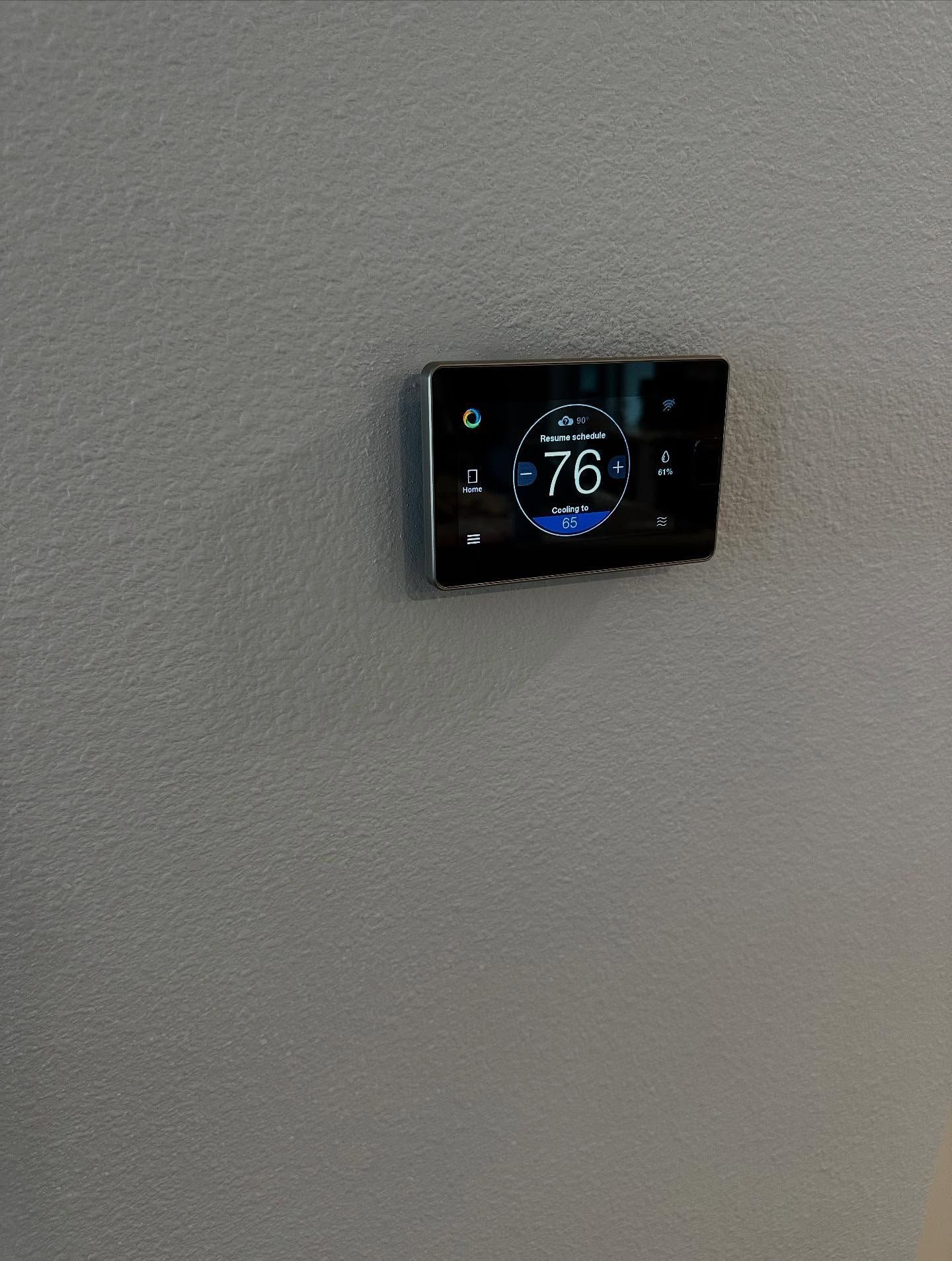 A wall-mounted, black smart thermostat displaying a temperature of 76 degrees Fahrenheit. It has a digital screen with blue and white accents.