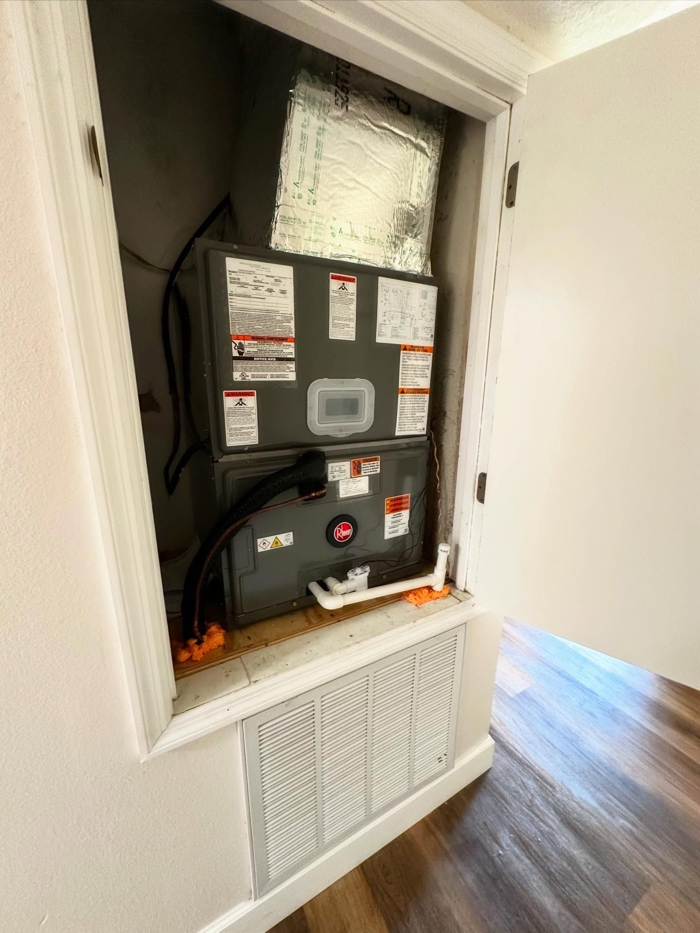 HVAC unit installed inside a closet. The unit is gray and has multiple warning labels. A white door is open.