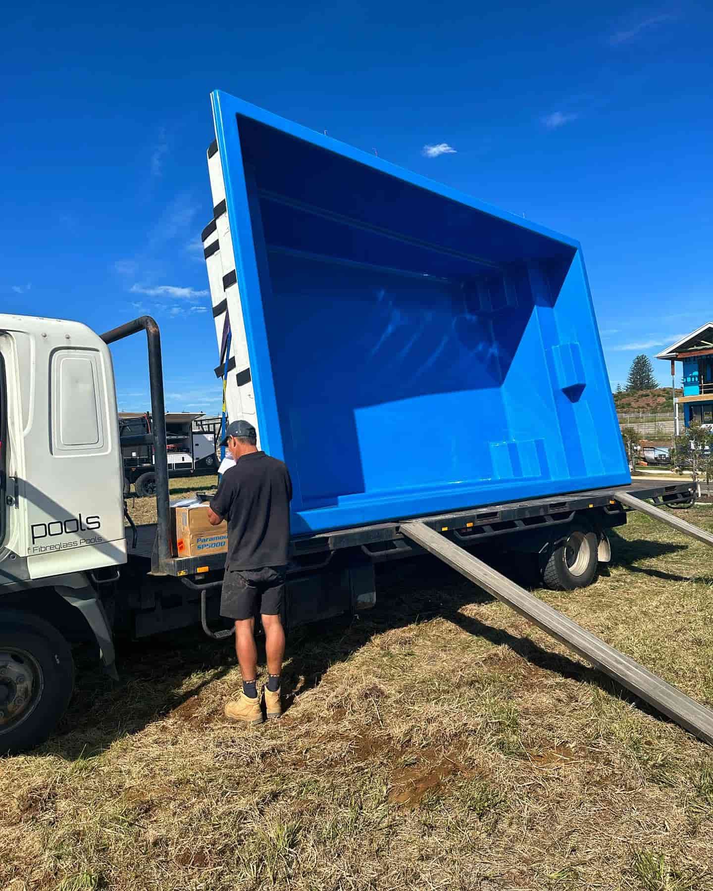 A man is standing next to a large blue swimming pool on the back of a truck.
