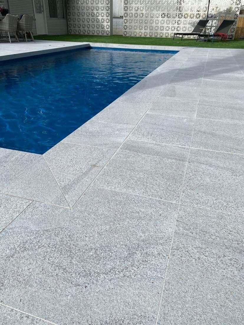 A swimming pool with a gray tiled floor and a blue water.