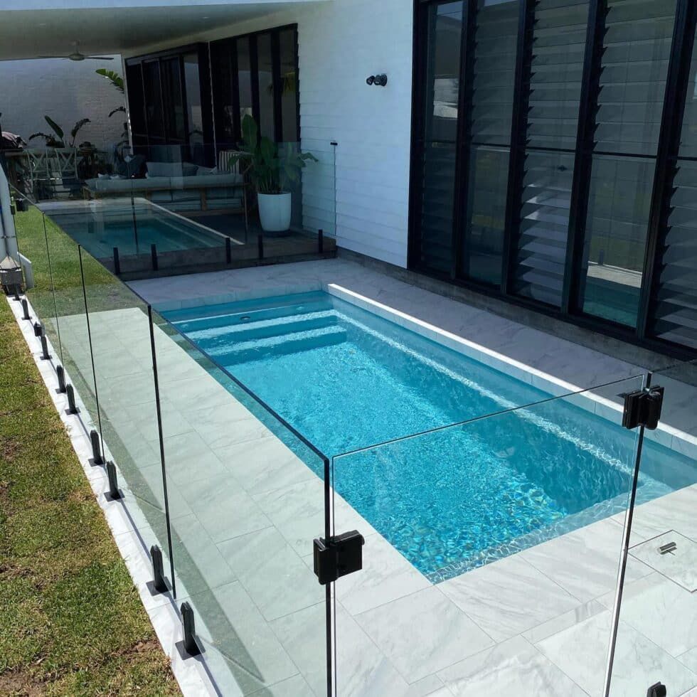 A Large Swimming Pool With A Glass Fence Around It — Evoke Pools In Lennox Head, NSW