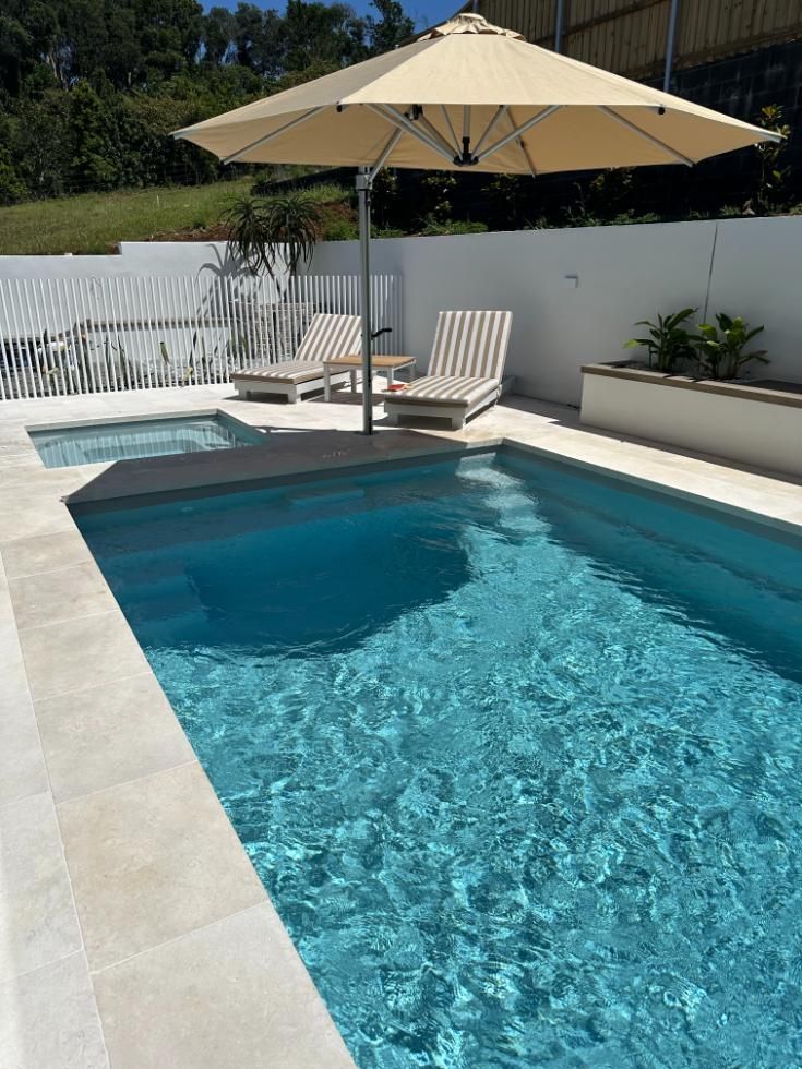 A large swimming pool with a large umbrella and chairs around it.