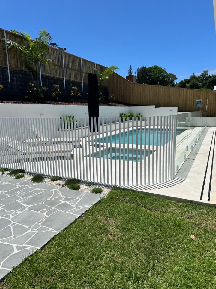 A white fence surrounds a swimming pool in a backyard.