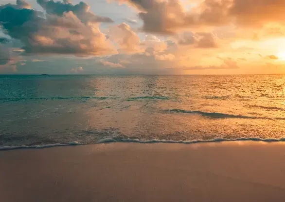 There is a sunset over the ocean and a beach in the foreground.