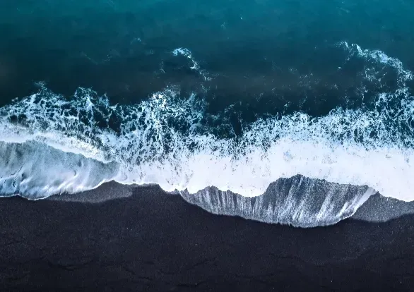 Aerial view of waves crashing on a black sandy beach.