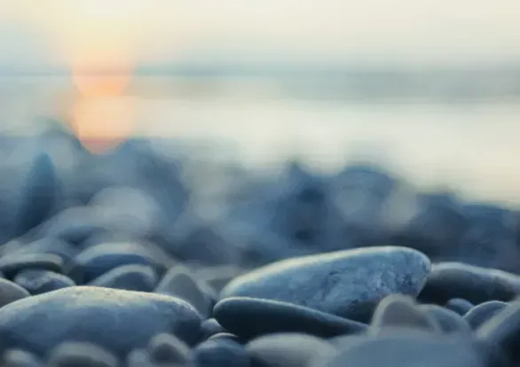 A pile of rocks on a beach with a sunset in the background.