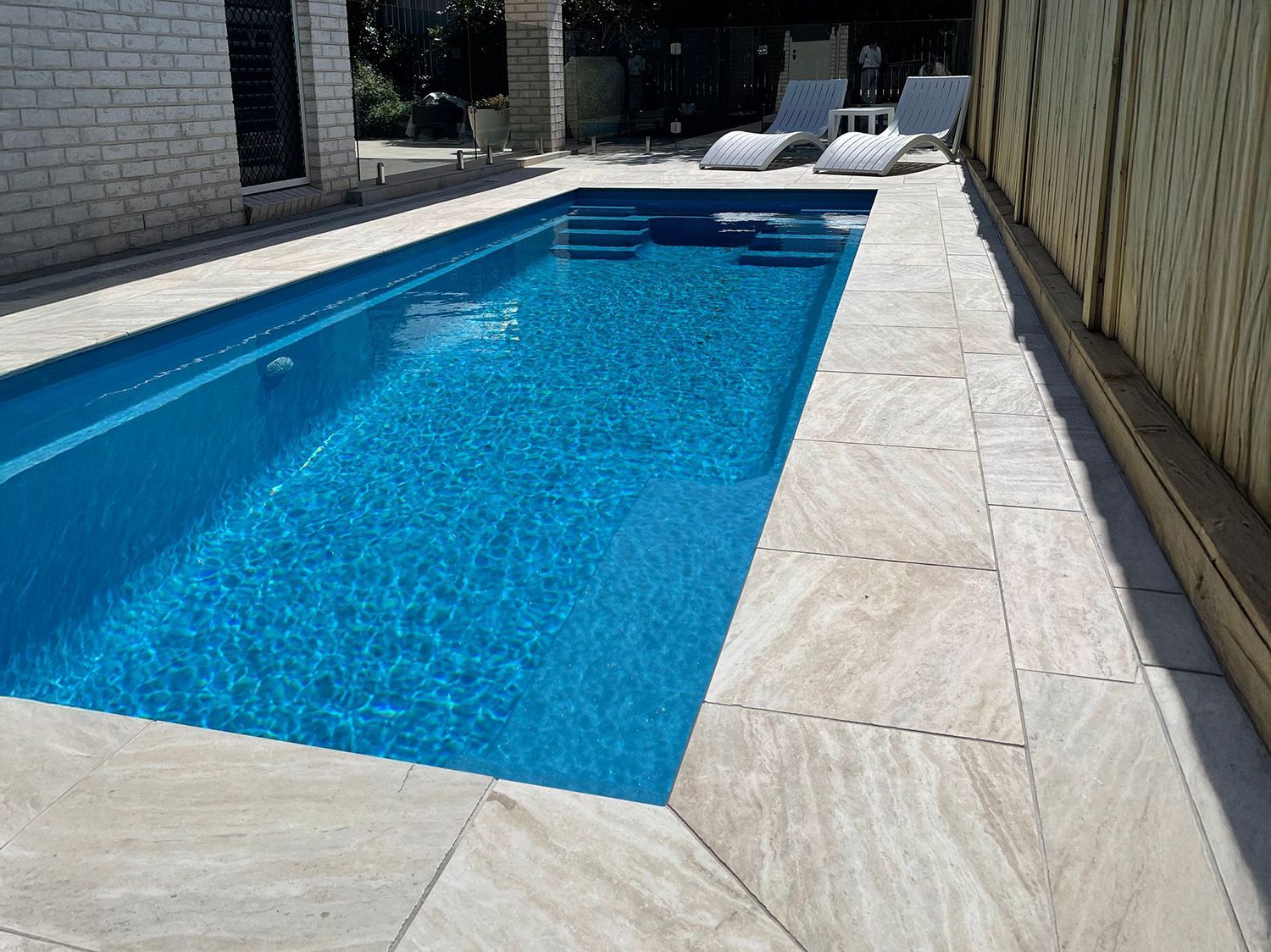 Rectangular Pool Next To A Light-Colored Patio And House
