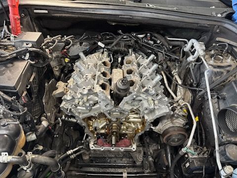 Car on a lift in a repair shop. The hood is open. Red lifts, tools, and parts on the floor.