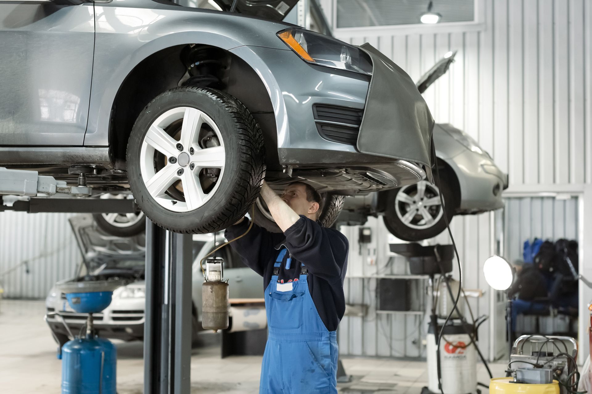 Mechanic working on a car raised on a lift in a repair shop.