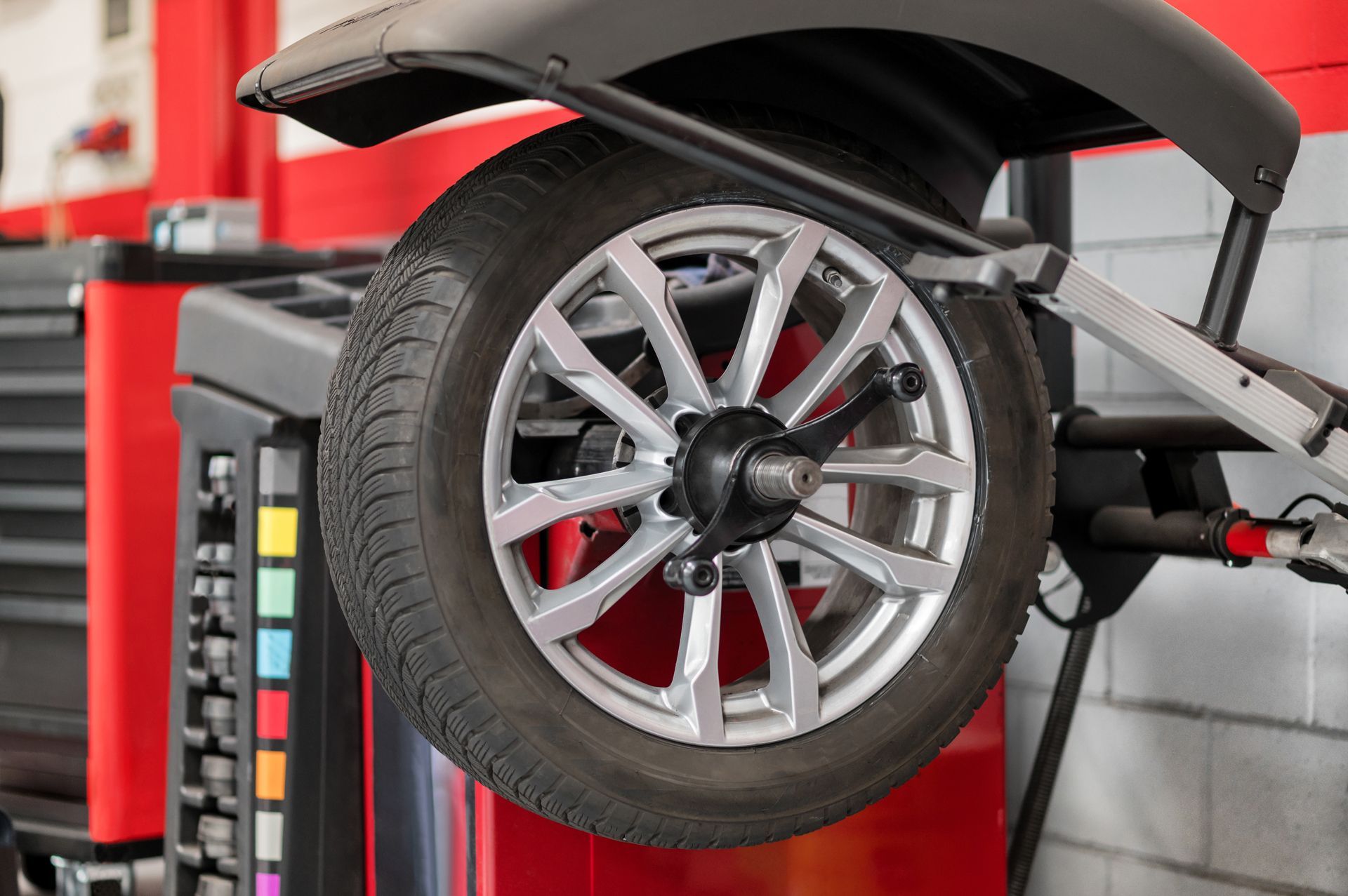 Tire on a balancing machine in a garage; black tire, silver rim, red and gray machine.