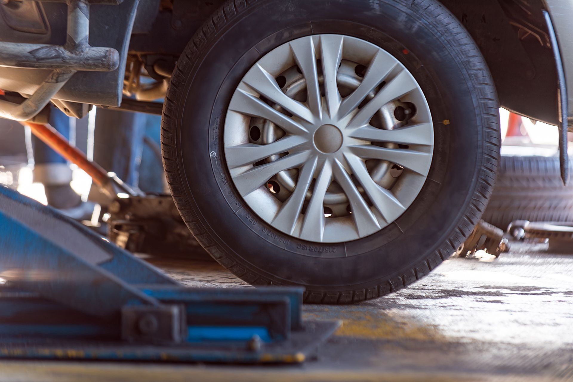Car tire on a vehicle lifted with a jack. The tire has a hubcap in a garage setting.