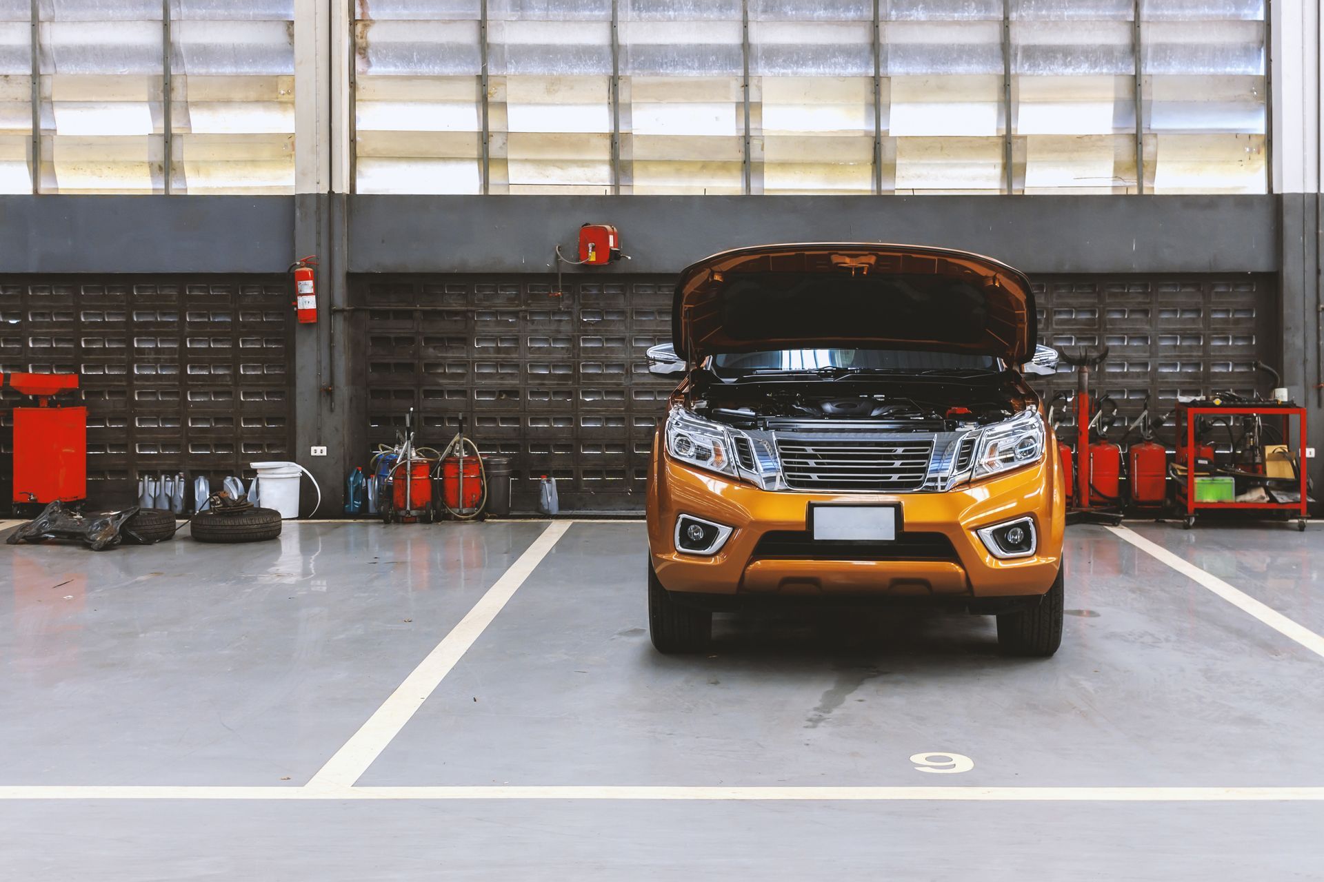 Orange SUV with open hood in a garage.