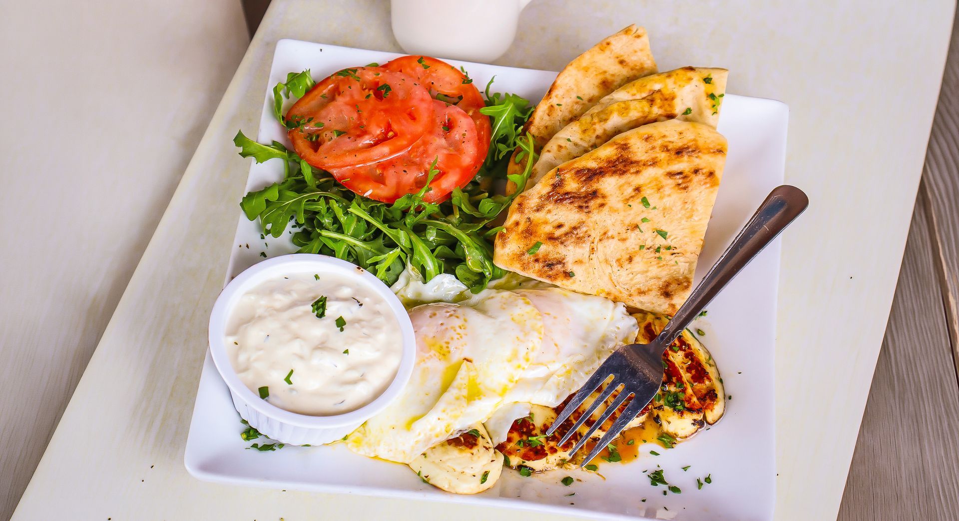 Grilled chicken, tomato, greens, and creamy dipping sauce in a takeout box with a fork