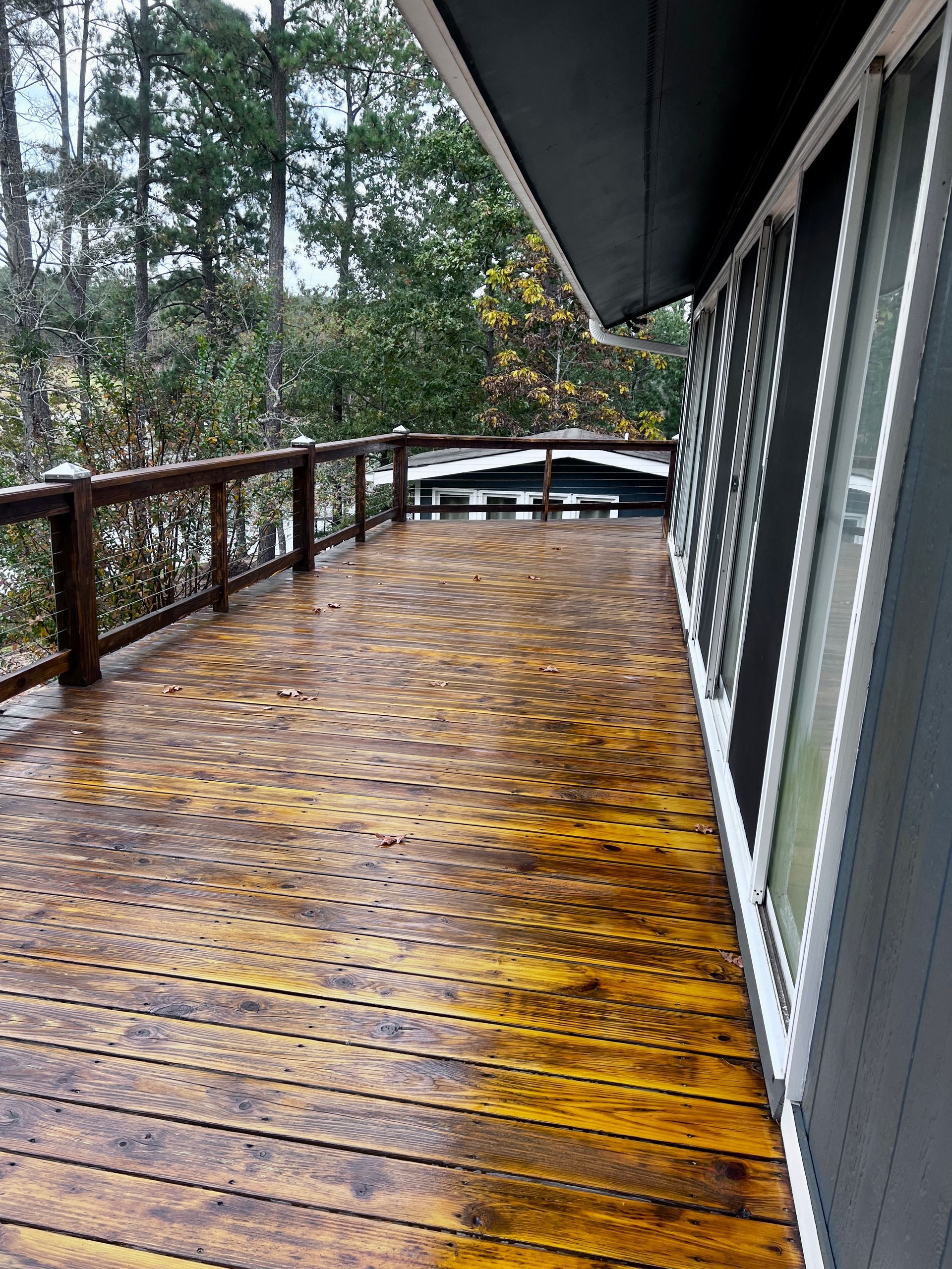 A large wooden deck on the side of a house with trees in the background.