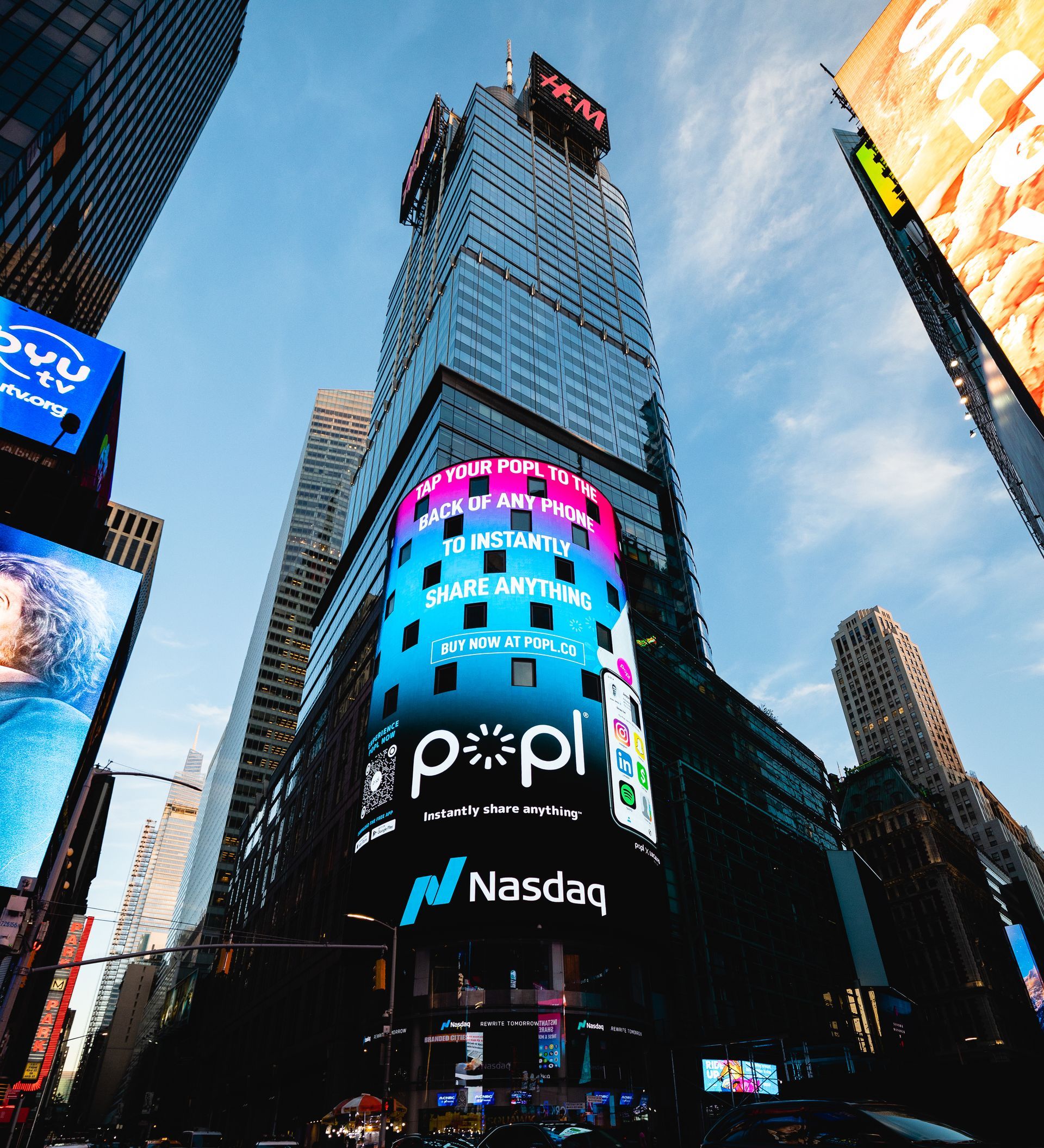 Nasdaq building in Times Square, NYC. Tall skyscraper with large digital displays. Blue sky, colorful ads.