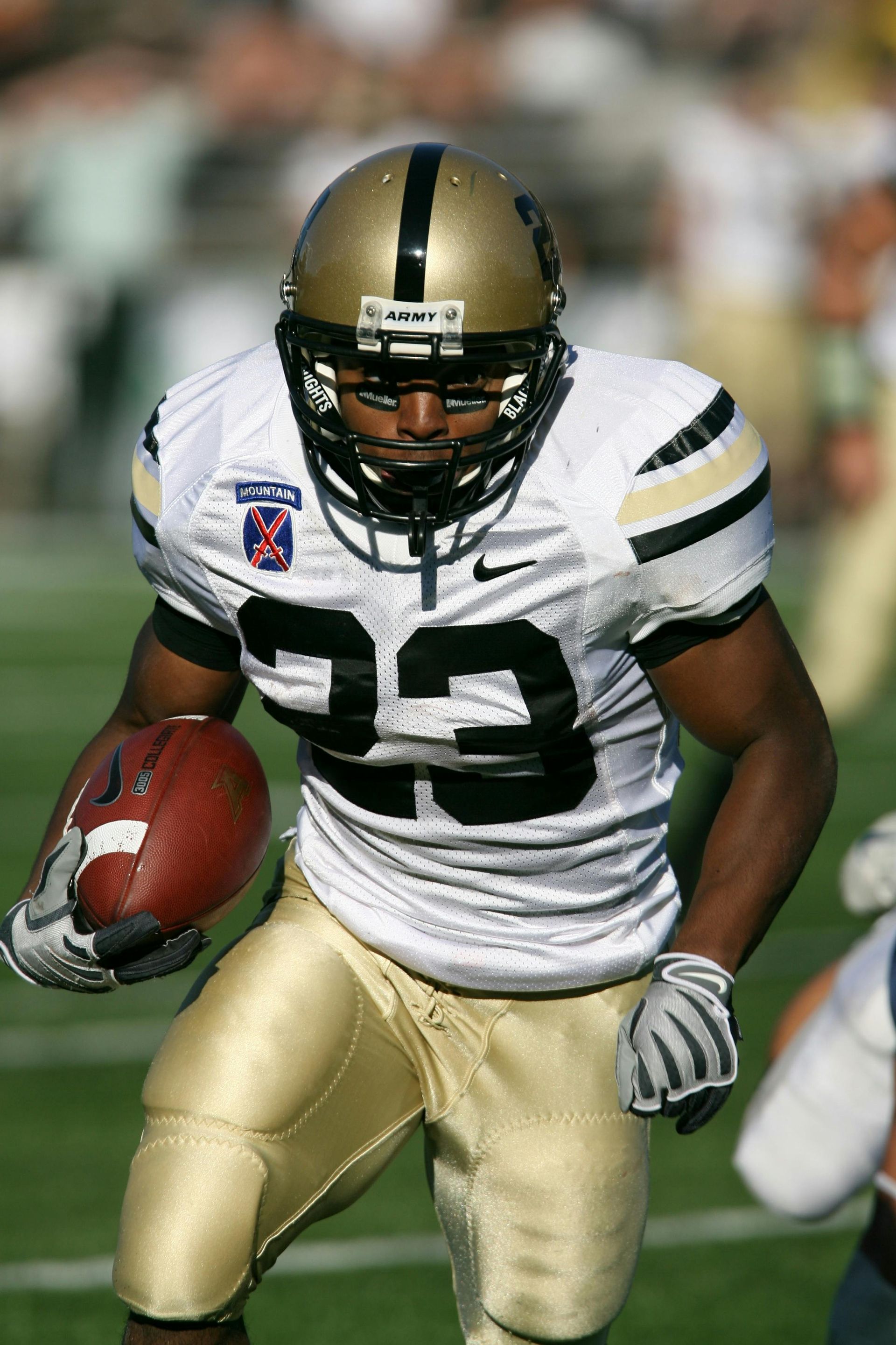 Football player in gold and white uniform carrying a ball, running on a field.
