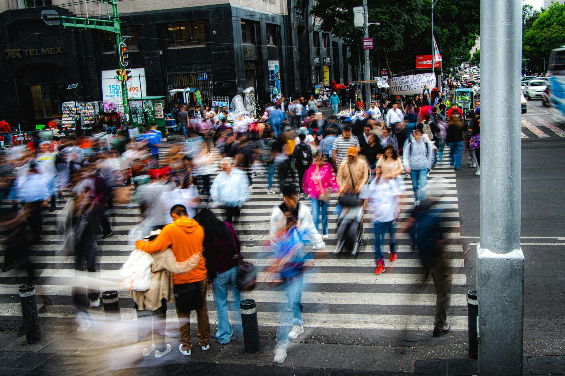 Crowd of people crossing a city street at a busy crosswalk, some blurred in motion.