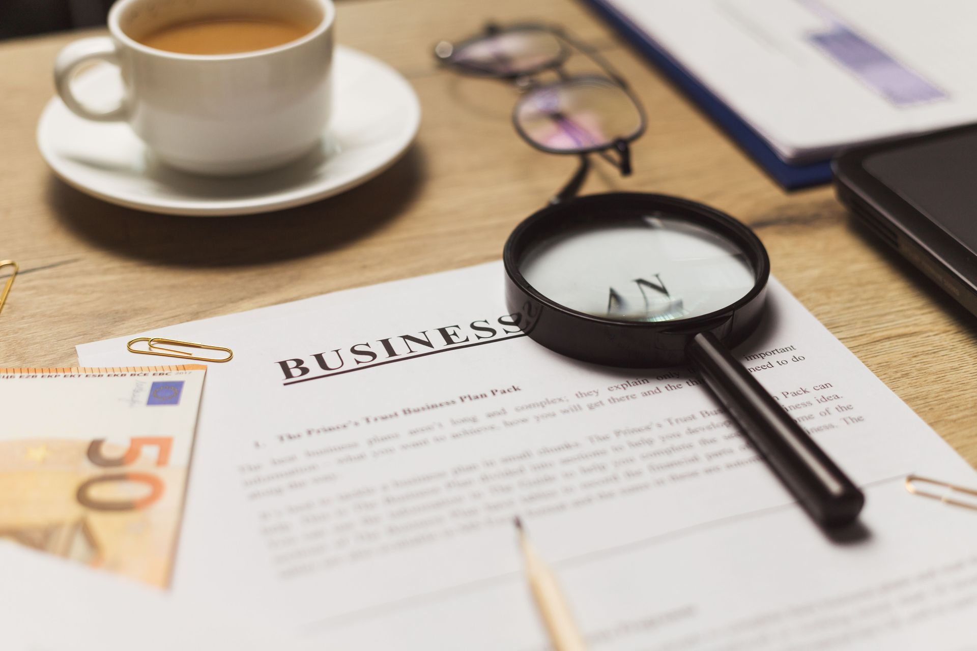 Business document with magnifying glass, coffee cup, eyeglasses, and notes on a desk