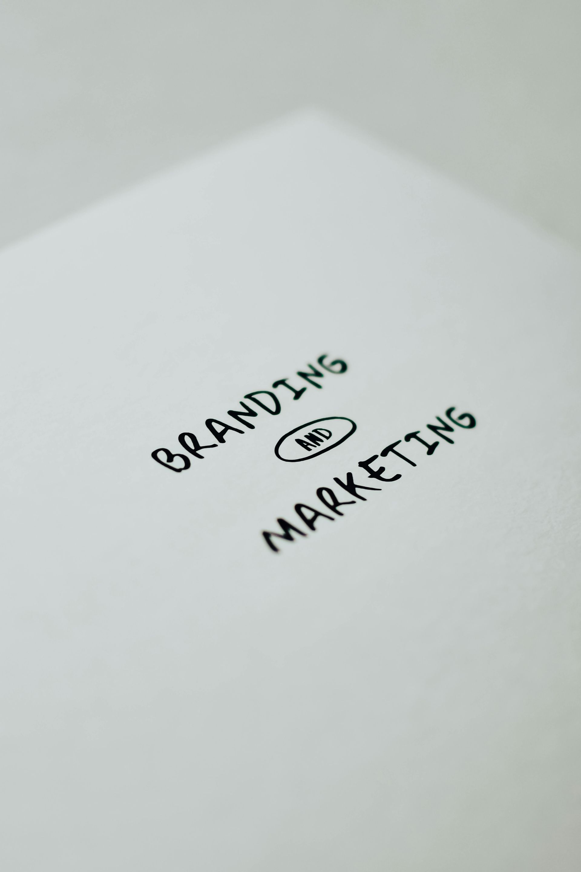 Handwritten “BRANDING” and “MARKETING” on white paper with “and” circled in black ink