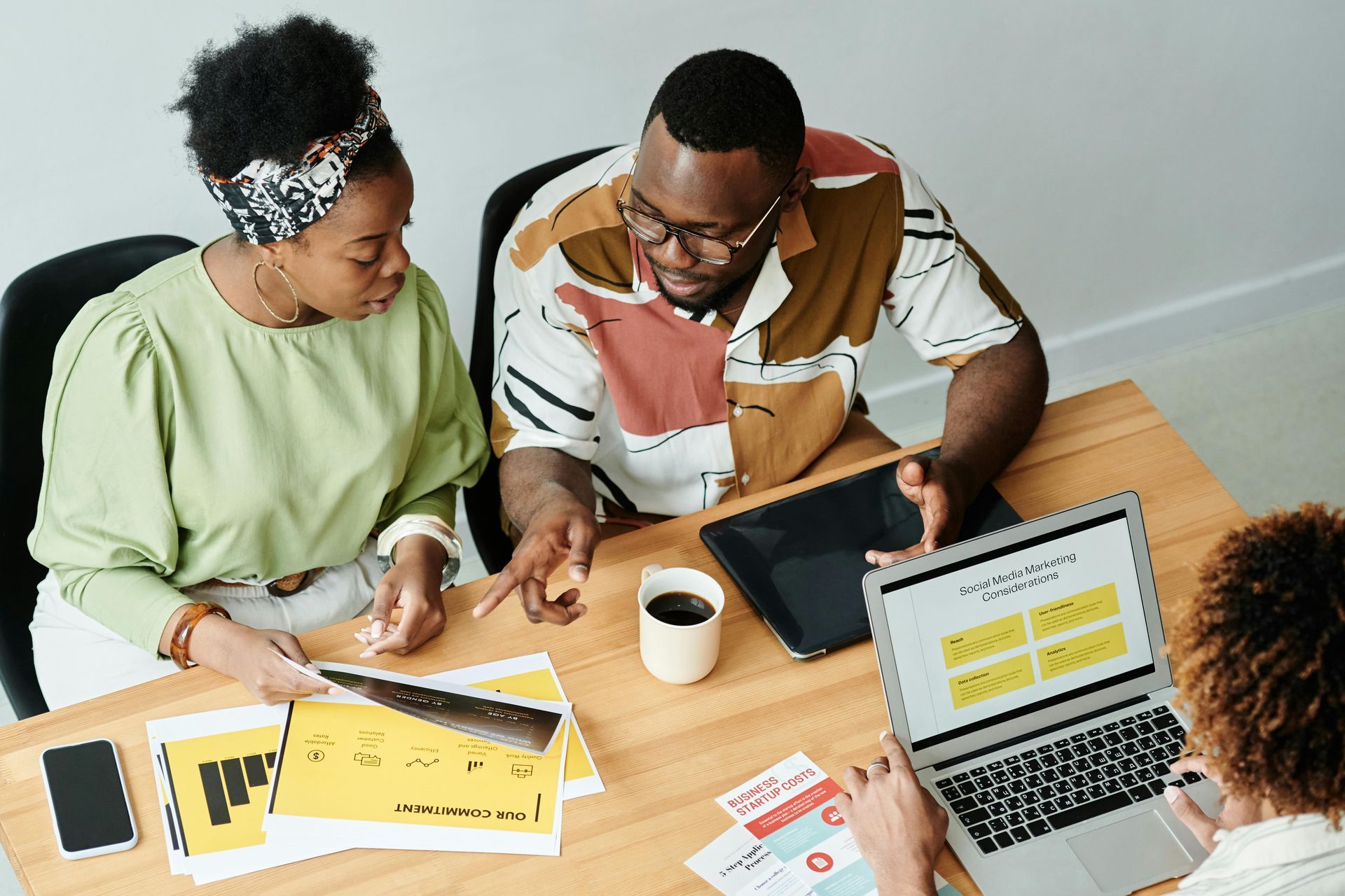 Two people reviewing documents and a laptop at a wooden table during a meeting