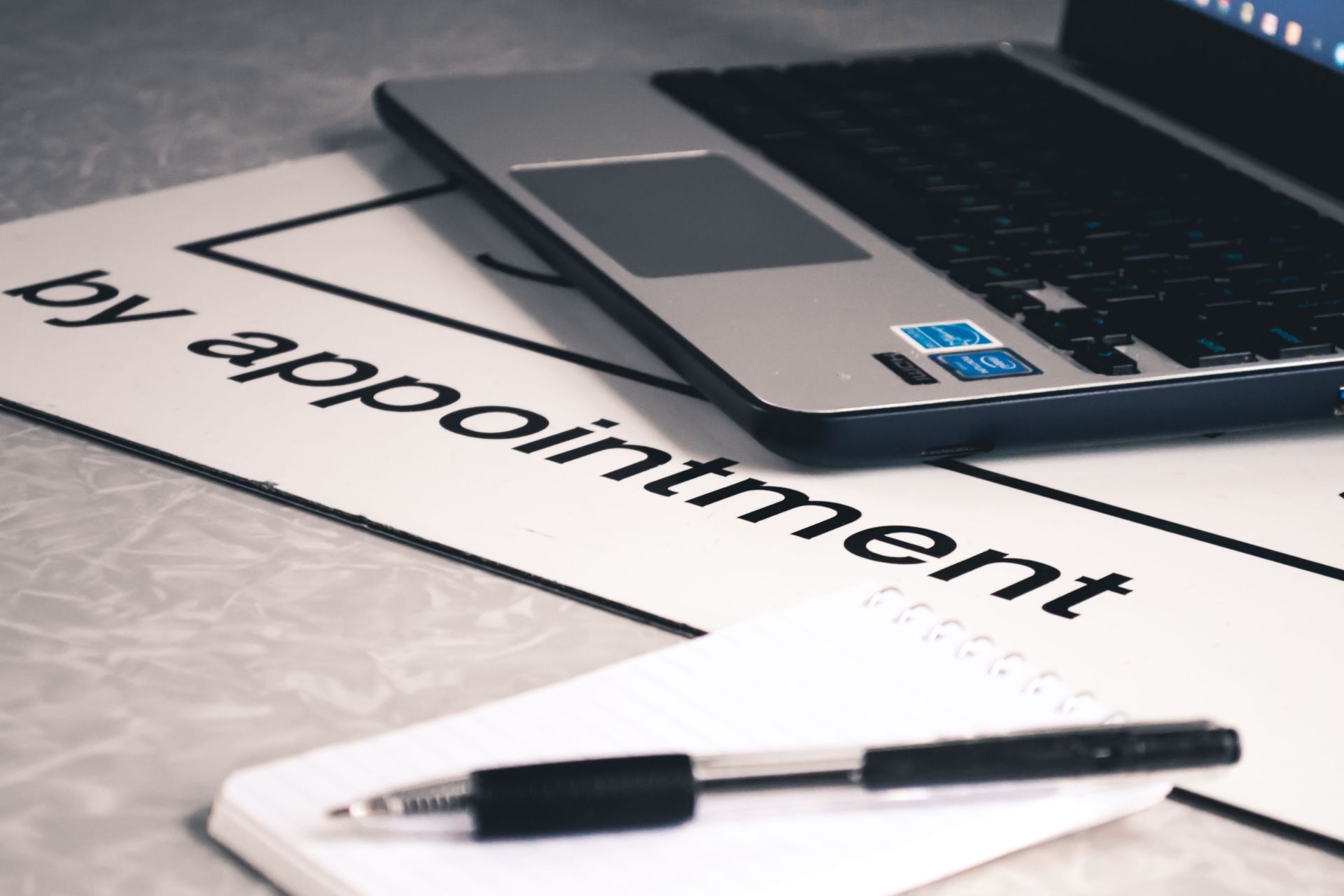 Laptop and pen on a desk beside a paper labeled “by appointment”