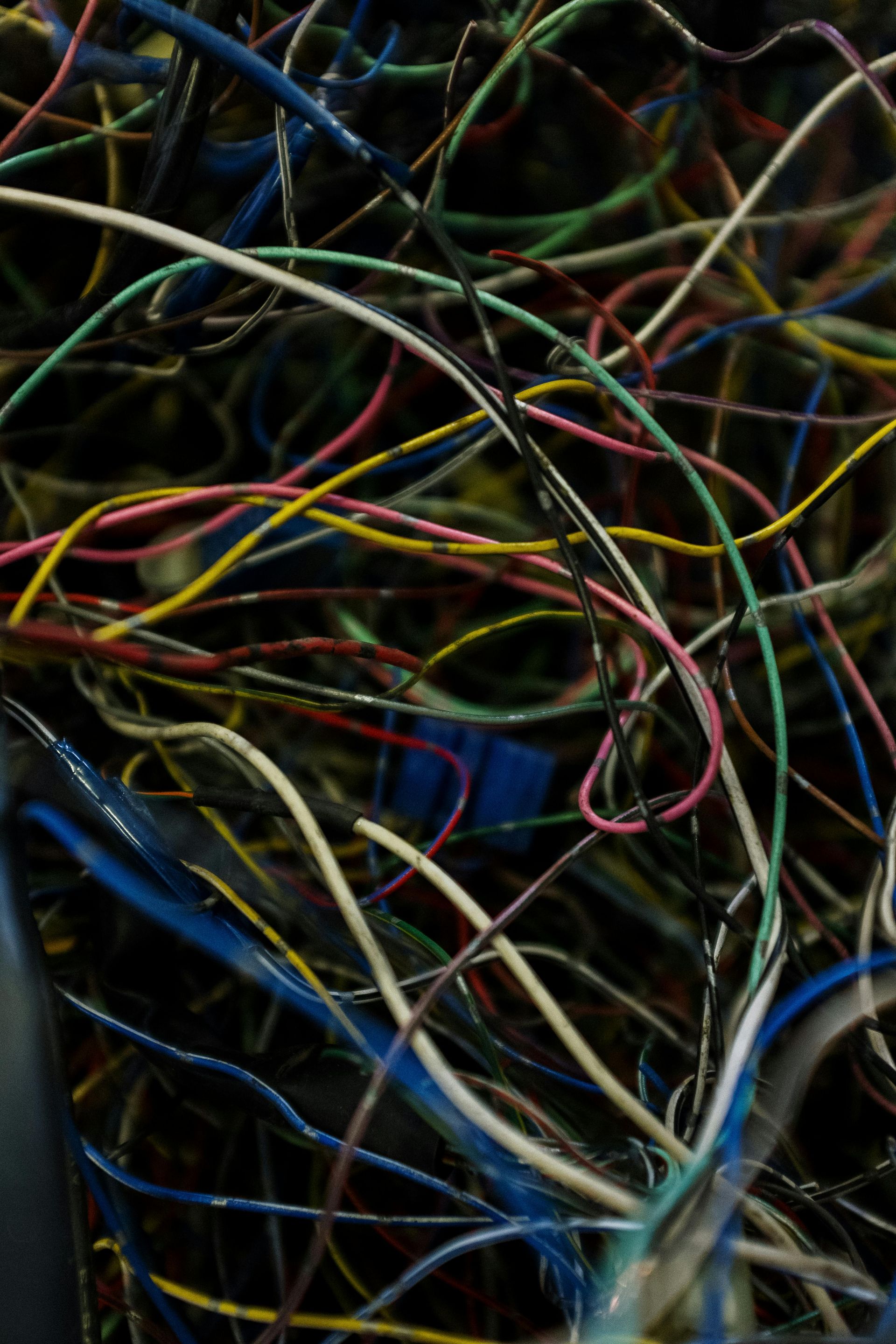 Tangled mass of colorful wires, including blue, yellow, green, and pink, against a dark background.