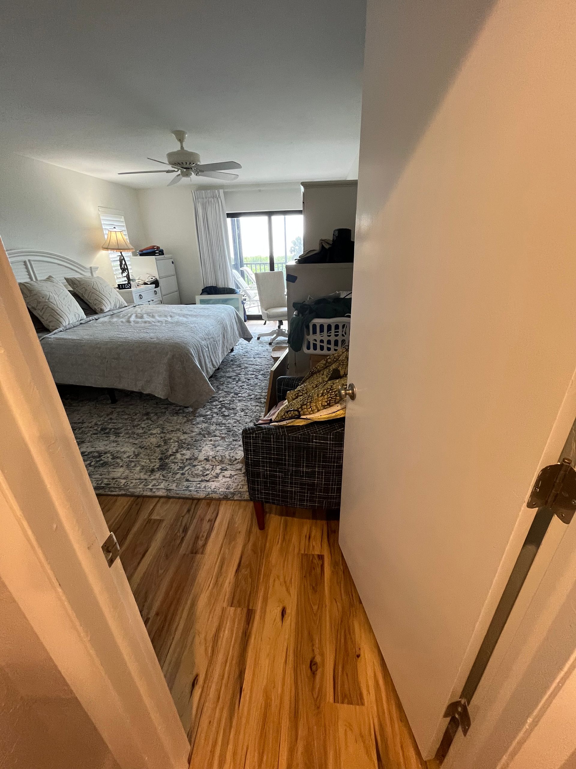 A hallway leading to a bedroom with hardwood floors and a bed.