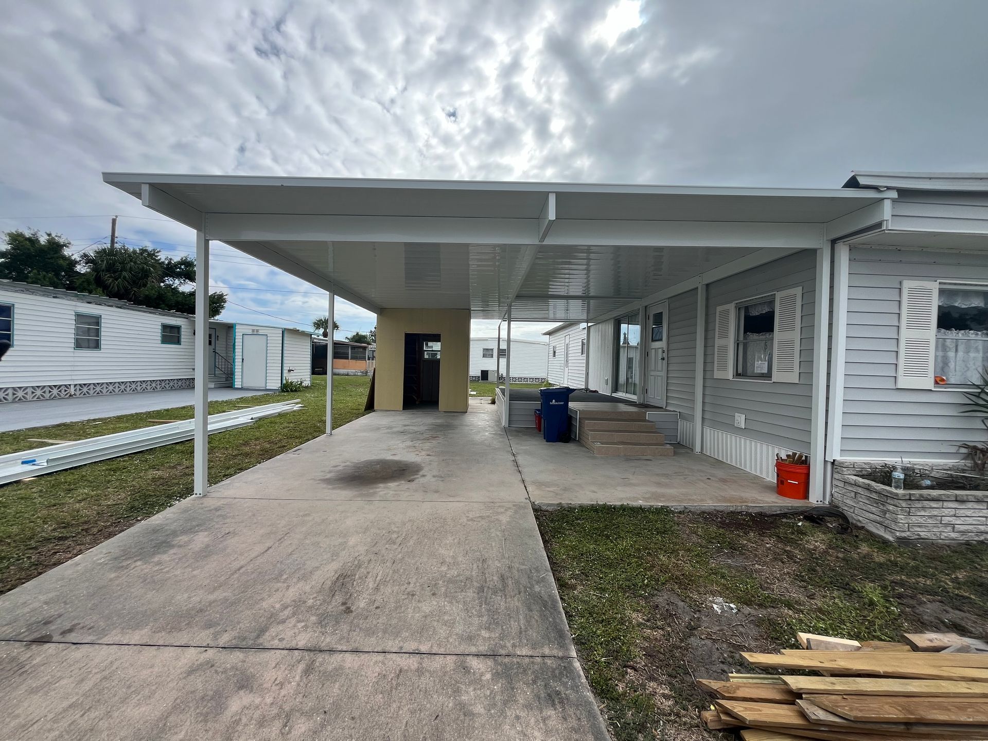 A mobile home with a covered driveway in front of it.