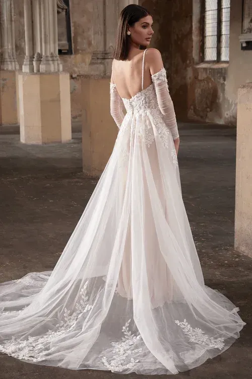 Woman in a white wedding dress with a long train, standing in an old building.